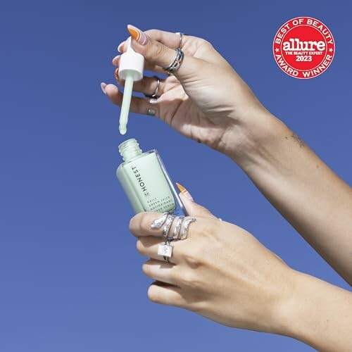 Hands holding a serum dropper bottle under blue sky, Allure 2023 award badge visible.